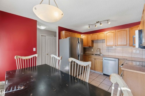 Kitchen featuring wood cabinetry, stainless steel refrigerator and dishwasher, tile flooring, and a tile backsplash - 14121 23 Street, Edmonton, AB 