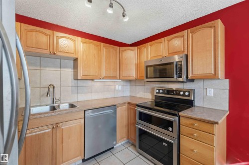 Modern kitchen featuring stainless steel appliances, light wood cabinetry, a double basin sink, and tile flooring - 14121 23 Street, Edmonton, AB 