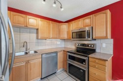 Modern kitchen featuring stainless steel appliances, light wood cabinetry, a double basin sink, and tile flooring - 