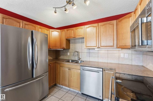 Kitchen featuring light wood cabinetry, stainless steel appliances, tiled backsplash, dual basin sink, and track lighting - 14121 23 Street, Edmonton, AB 
