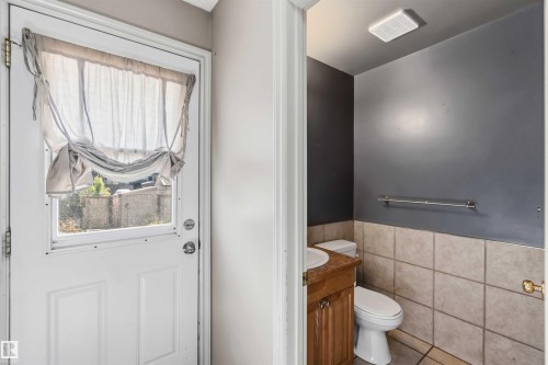 Powder room featuring a wood-finish vanity with a white basin sink, a toilet, and ceramic tile wainscoting - 14121 23 Street, Edmonton, AB 
