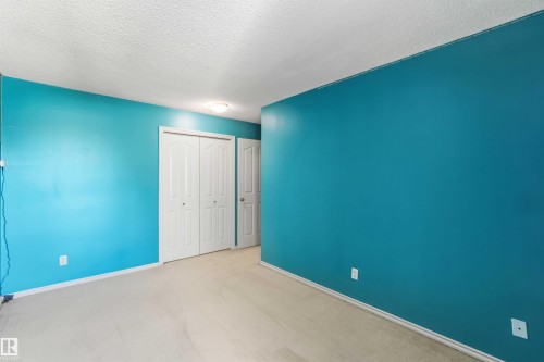 Room featuring light-colored carpeting, vibrant blue wall paint, white trim, and a flush-mounted ceiling light fixture - 14121 23 Street, Edmonton, AB 