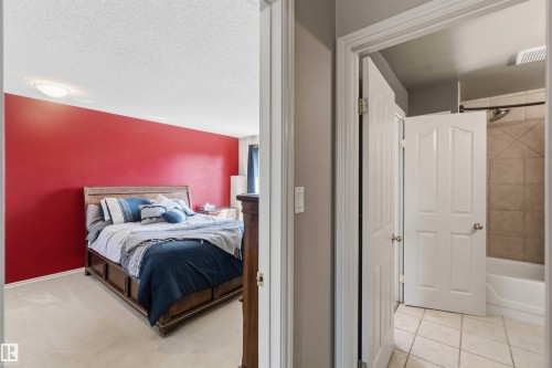 Bedroom with carpet flooring and a bold red accent wall, featuring a nearby bathroom with tiled flooring and a shower-over-tub combination - 14121 23 Street, Edmonton, AB 