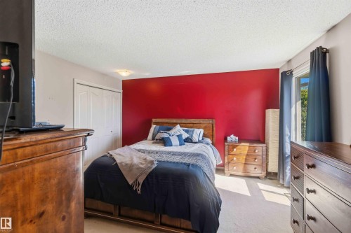 Bedroom featuring a red accent wall, light-toned carpet flooring, and a window with dark curtains - 14121 23 Street, Edmonton, AB 