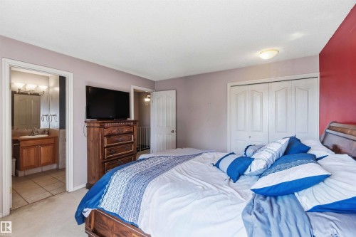 Spacious bedroom featuring light lavender walls, white bi-fold closet doors, and direct access to a private bathroom with a wooden vanity and tile flooring - 14121 23 Street, Edmonton, AB 
