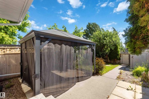 Backyard space featuring a covered gazebo with mesh screens, concrete patio, and mature perimeter trees - 14121 23 Street, Edmonton, AB 