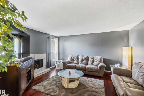 Living space featuring rich wood-finish flooring, a tiled fireplace, and neutral wall tones - 14121 23 Street, Edmonton, AB 
