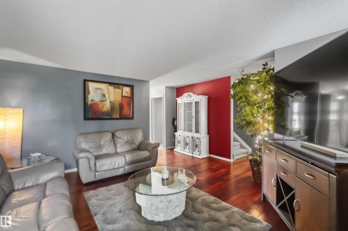 Spacious living area featuring rich wood-finish flooring, a contemporary accent wall, and a built-in display cabinet - 14121 23 Street, Edmonton, AB 