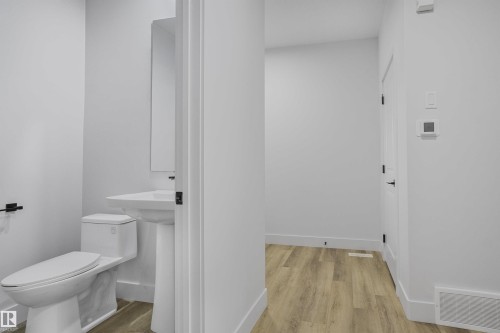 Powder room featuring a pedestal sink, wall-mounted mirror, and a modern toilet - 1915 164 Street, Edmonton, AB 