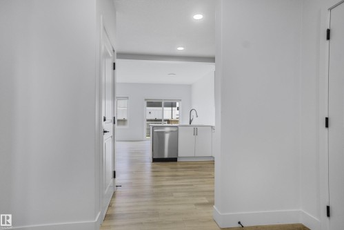 Modern kitchen featuring stainless steel appliances, light wood-finish flooring, recessed lighting, white cabinetry, and a contemporary faucet - 1915 164 Street, Edmonton, AB 