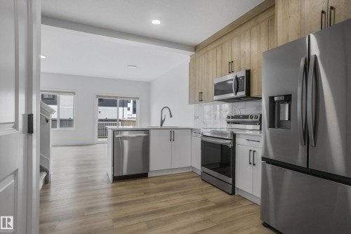 Contemporary kitchen featuring stainless steel appliances, light wood-finish cabinetry, white lower cabinetry, an island with a built-in dishwasher, and a tile backsplash - 1915 164 Street, Edmonton, AB 