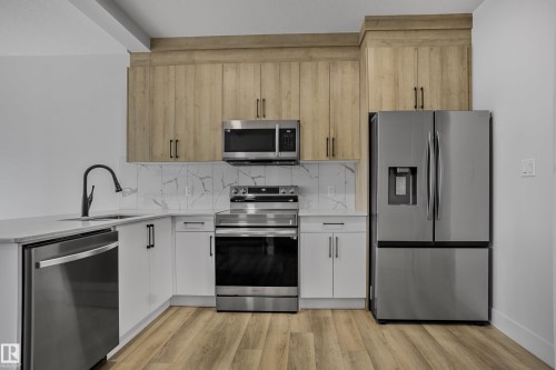 Kitchen featuring stainless steel appliances, wood-finish flooring, white cabinetry, light countertops, and a full-height tile backsplash - 1915 164 Street, Edmonton, AB 