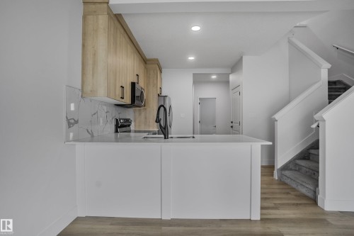Modern kitchen with white shaker-style base cabinetry, light wood-finish upper cabinetry, white countertops, and a full-height marble-look backsplash - 1915 164 Street, Edmonton, AB 