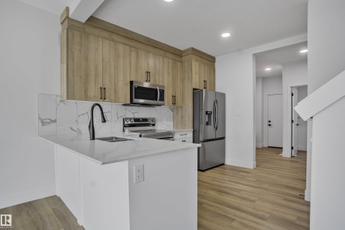Kitchen featuring light wood-finish cabinetry, stainless steel appliances, a white countertop, a black gooseneck faucet, and a white tile backsplash - 1915 164 Street, Edmonton, AB 