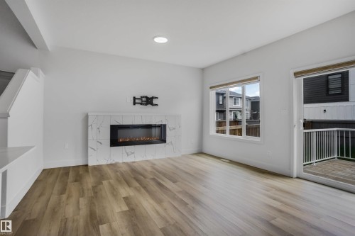 Contemporary living area with wood-finish flooring and a linear electric fireplace featuring a white marble-look tile surround - 1915 164 Street, Edmonton, AB 