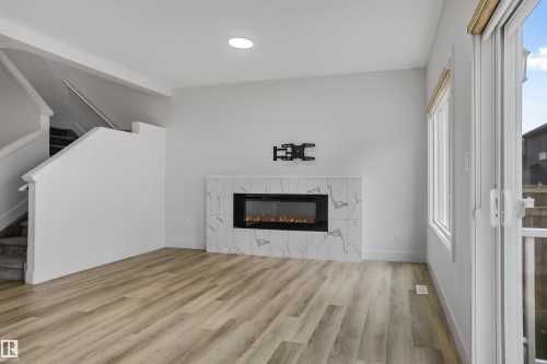 Living area featuring wood-finish flooring, a contemporary electric fireplace with a marble-look surround, recessed lighting, and a sliding glass door opening to an exterior balcony - 1915 164 Street, Edmonton, AB 