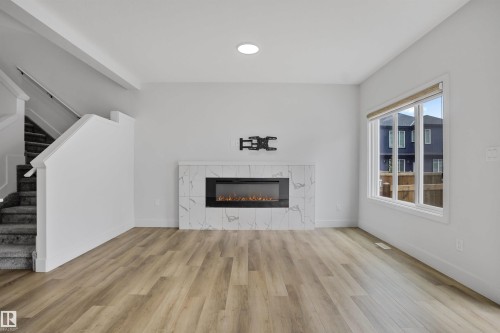 Living area featuring a contemporary fireplace with a marble-look surround, wood-finish flooring, and a large window - 1915 164 Street, Edmonton, AB 