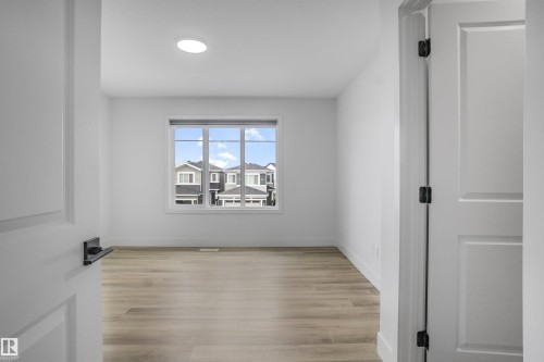 Room featuring wood-finish flooring, a large window, a circular recessed light fixture, and white painted walls - 1915 164 Street, Edmonton, AB 