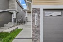 Modern garage door with horizontal window panel and a stone-clad pillar featuring vertical house numbers - 1915 164 Street, Edmonton, AB 