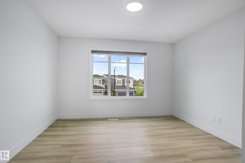 Bright interior space featuring a large window, light wood-finish flooring, white baseboards, and a flush-mount ceiling light - 1915 164 Street, Edmonton, AB 