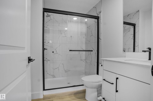 Modern bathroom featuring a glass-enclosed shower with black framing, white veined tile, and a black rainfall showerhead - 1915 164 Street, Edmonton, AB 