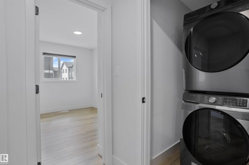 Stackable laundry appliances in a dedicated utility space, featuring light wood-finish flooring and a white color palette - 1915 164 Street, Edmonton, AB 