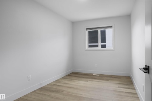 Room featuring wood-finish flooring, white baseboards, a white window frame, and a dark window treatment - 1915 164 Street, Edmonton, AB 