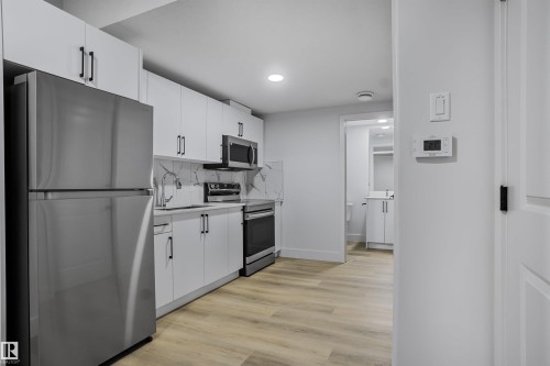 Modern kitchen featuring white cabinetry, stainless steel appliances, wood-finish flooring, and a patterned backsplash - 1915 164 Street, Edmonton, AB 