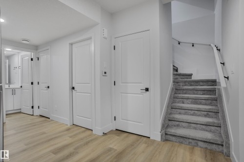 Wood-finish flooring extending into a hallway featuring multiple paneled doors with matte black hardware - 1915 164 Street, Edmonton, AB 