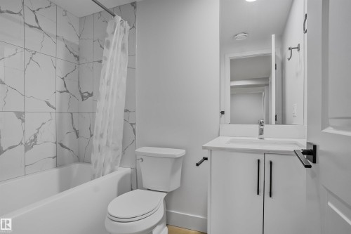 Bathroom featuring a white vanity with a recessed sink, a framed mirror, a toilet, a full bathtub, and tiled walls - 1915 164 Street, Edmonton, AB 