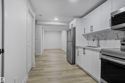 Modern kitchen featuring white cabinetry, stainless steel appliances, a white quartz-finish countertop, and a white tile backsplash with grey veining - 1915 164 Street, Edmonton, AB 
