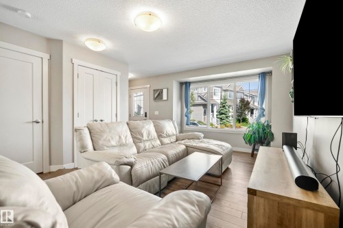 Living area featuring wood-finish flooring, a large bay window, white baseboards, and two flush-mount ceiling lights - 11 4205 30 Street, Edmonton, AB 