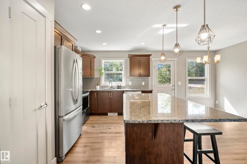 Kitchen featuring wood-finish flooring, recessed lighting, stainless steel appliances, dark wood cabinetry, and a granite-topped island with pendant lighting - 11 4205 30 Street, Edmonton, AB 