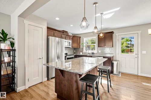 Kitchen featuring wood-finish flooring, dark wood cabinetry, stainless steel appliances, and a granite island with seating - 11 4205 30 Street, Edmonton, AB 
