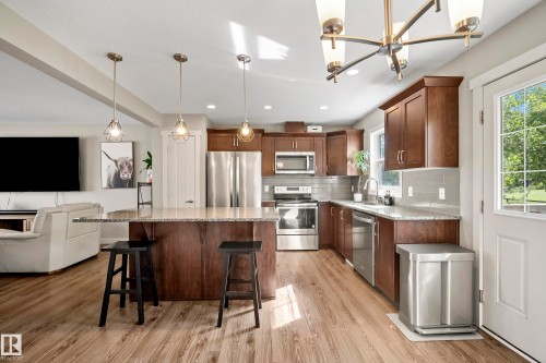 Spacious kitchen featuring an island with pendant lighting, wood-finish flooring, stainless steel appliances, dark wood cabinetry, and light-toned countertops - 11 4205 30 Street, Edmonton, AB 