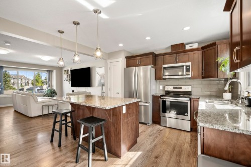 Open-concept kitchen featuring an island with a light-toned countertop, wood-finish flooring, dark wood cabinetry, stainless steel appliances, and pendant lighting - 11 4205 30 Street, Edmonton, AB 
