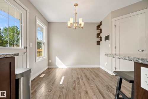 Spacious dining area featuring wood-finish flooring, a contemporary chandelier, built-in corner shelving, and light-toned walls - 11 4205 30 Street, Edmonton, AB 