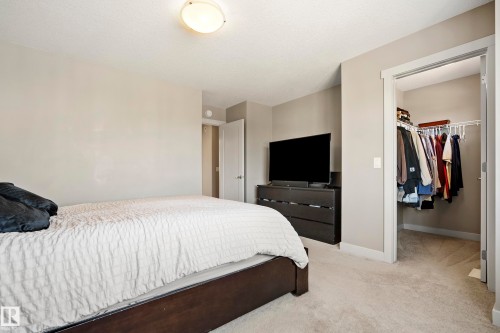 Neutral-toned bedroom featuring wall-to-wall carpeting and an open closet with built-in shelving and hanging rods - 11 4205 30 Street, Edmonton, AB 