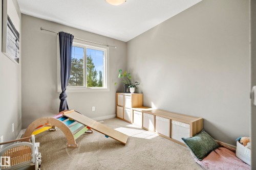 Carpeted room with a single window featuring white trim and blue drapes - 11 4205 30 Street, Edmonton, AB 