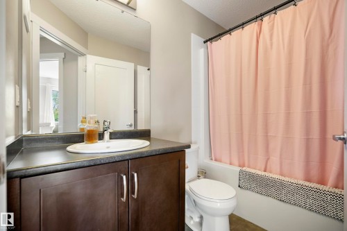 Bathroom featuring an integral sink vanity with a dark wood-finish cabinet, dark countertop, and a full-width mirror - 11 4205 30 Street, Edmonton, AB 