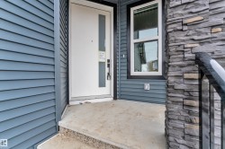 Entryway featuring a white door with a vertical glass insert, blue horizontal siding, stone veneer accents, a window with dark trim, and a concrete stoop - 