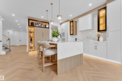 Modern kitchen featuring a waterfall island with slatted wood paneling, herringbone wood-finish flooring, white cabinetry, integrated appliances, and a marble-patterned backsplash - 