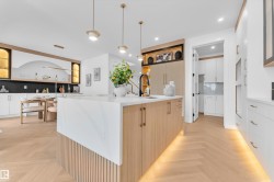 Kitchen featuring a waterfall island with a grooved wood-finish base, integrated under-cabinet lighting, and a matte black faucet - 