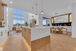 Open-concept kitchen and living area featuring high ceilings, herringbone wood-finish flooring, a waterfall island with fluted wood paneling, and an integrated dining space with built-in cabinetry - 
