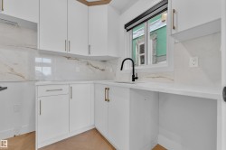 Modern kitchen featuring white cabinetry, gold-tone hardware, a black gooseneck faucet, light countertops, and a full-height backsplash with veining - 