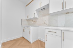 White cabinetry with brass hardware, light-toned countertops, and a marbled backsplash - 