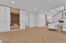 Entryway featuring custom built-in cabinetry with white and wood-finish doors, an integrated seating area with slatted wood-finish paneling, and herringbone-pattern wood-finish flooring - 