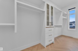 Walk-in closet featuring built-in white cabinetry, glass-front upper cabinets, and three drawers with brass hardware - 