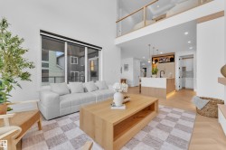 Open-concept living space featuring high ceilings, wood-finish herringbone flooring, a kitchen island with stone countertop, and a second-story loft with glass railing - 