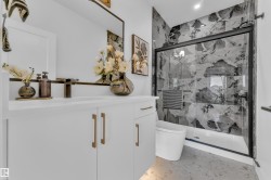 Modern bathroom featuring a white vanity with gold-tone hardware, a rectangular mirror with a dark frame, a contemporary toilet, and a glass-enclosed shower with black-framed sliding doors and large format patterned wall tiles - 